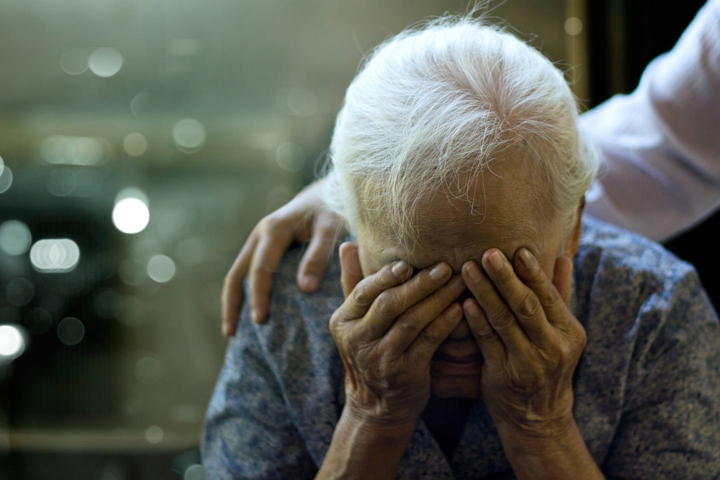An older person crying with hands over their eyes