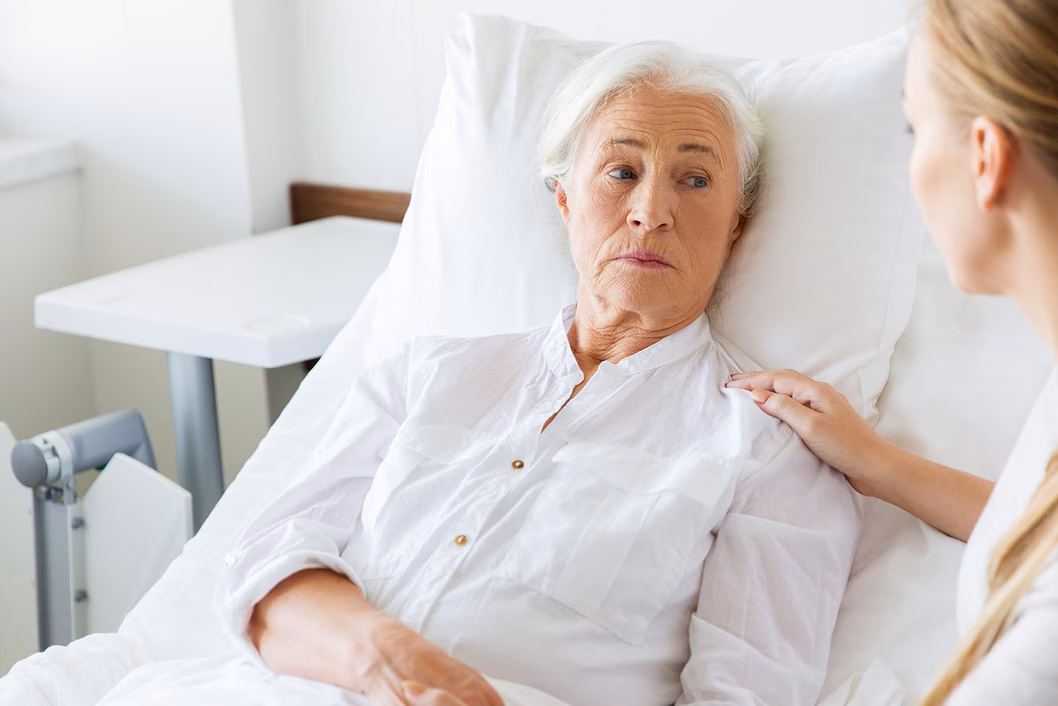 Photo of a woman in white in a hospital bed with a nurse attending