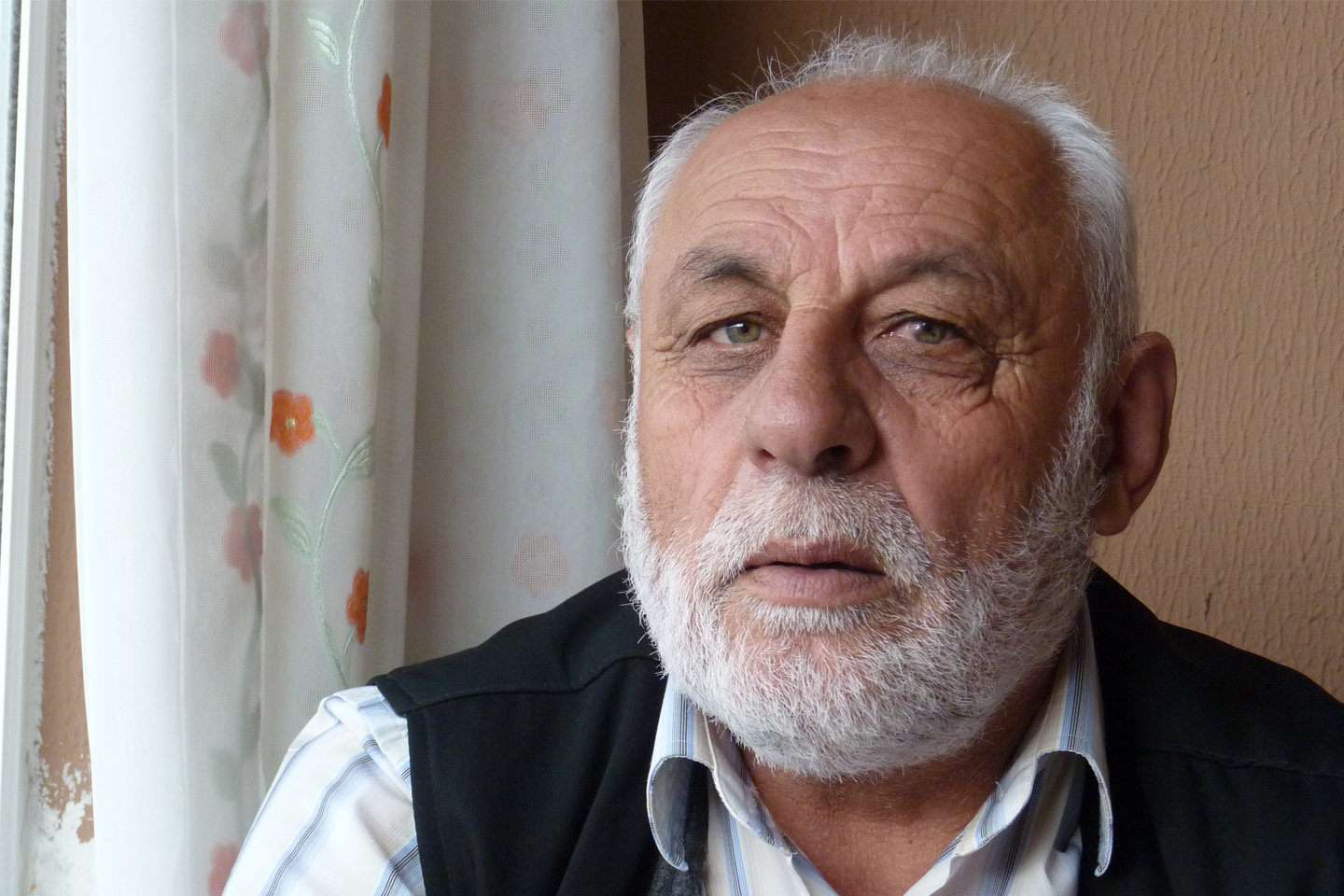 Image of an older bearded man who is sitting inside near a window