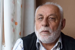 Image of an older bearded man who is sitting inside near a window