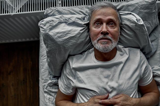 Photo of a man in a white T shirt lying on a bed