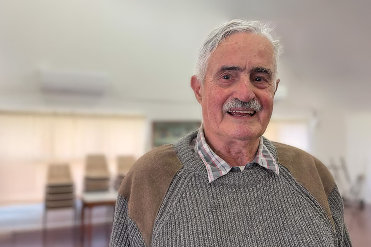 Photo of a smiling man in a taupe and grey jumper