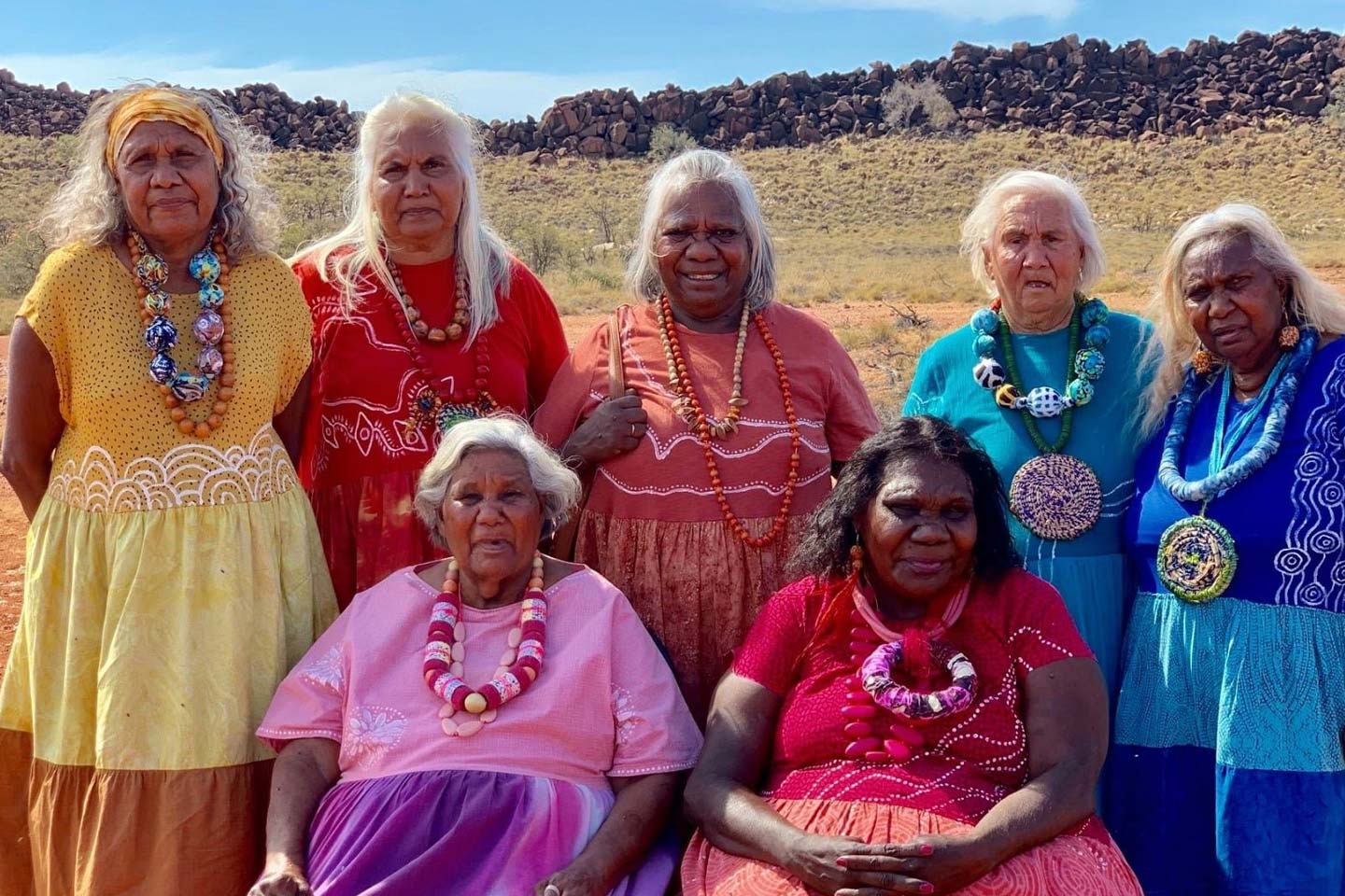 Photo of indigenous elder women wearing gorgeous coloured dresses and jewellery in a desert landscape