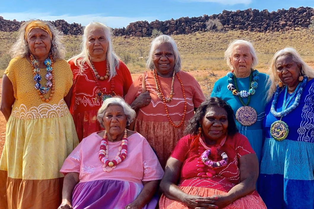 Photo of indigenous elder women wearing gorgeous coloured dresses and jewellery in a desert landscape