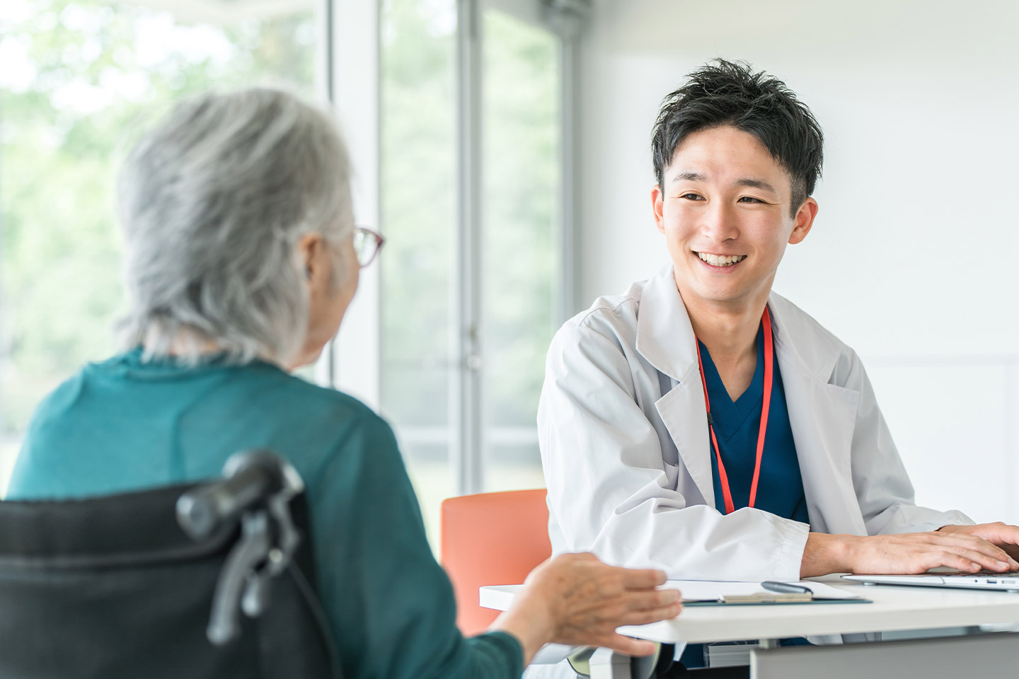 Photo of young man in a white coat smiling at a woman in a wheelchair