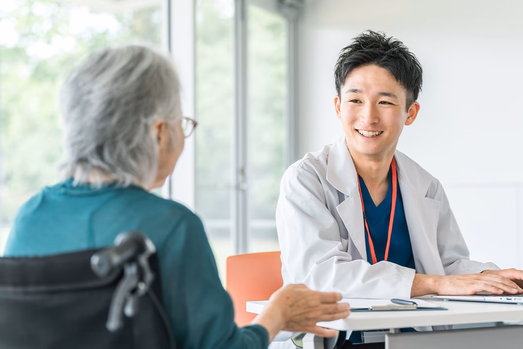 Photo of young man in a white coat smiling at a woman in a wheelchair