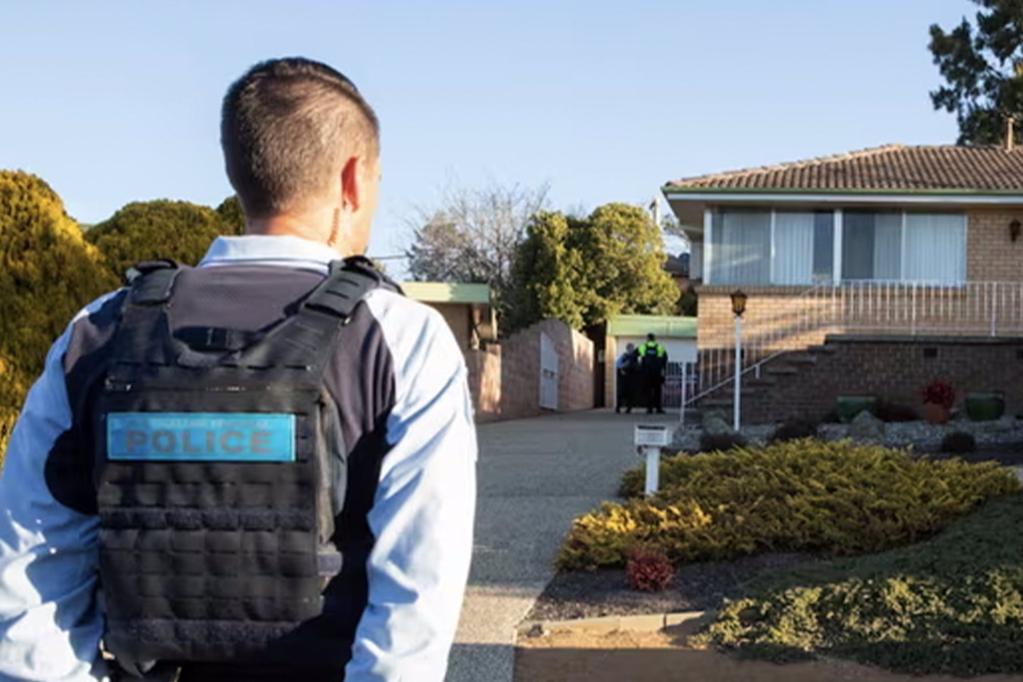 Photo of a police officer standing in front of a cream brick home