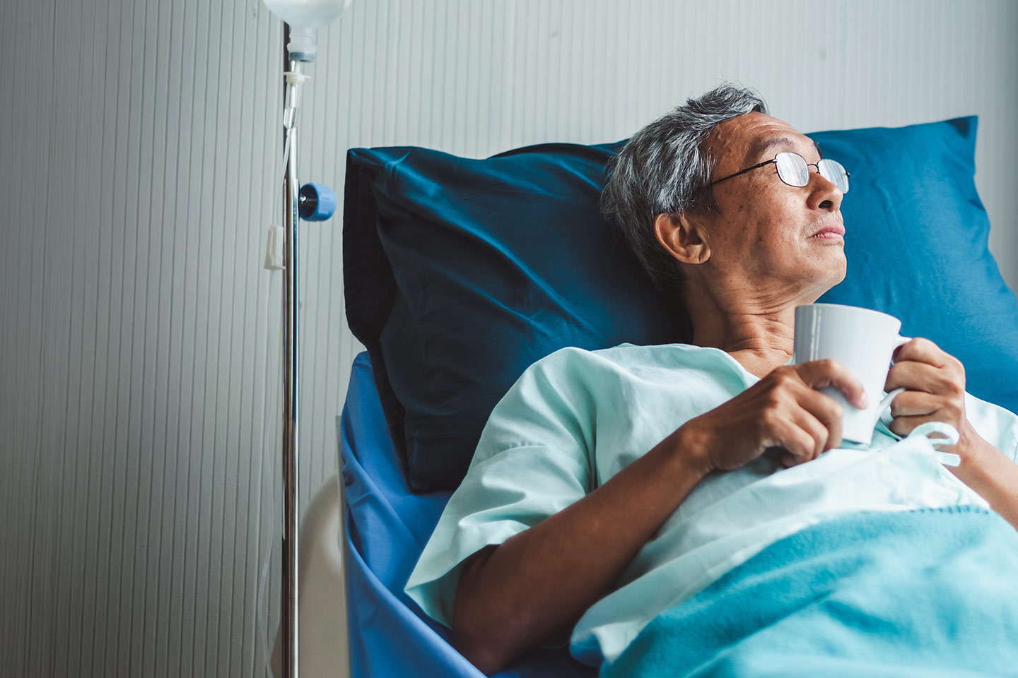 Photo of a man drinking from a cup in a hospital bed