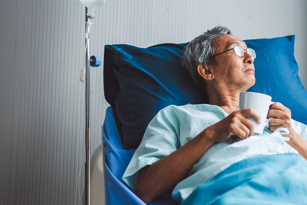 Photo of a man drinking from a cup in a hospital bed