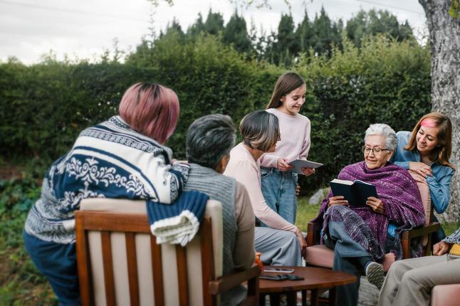 Image of a large intergenerational family in a backyard sitting around a grandmother who is reading from a book