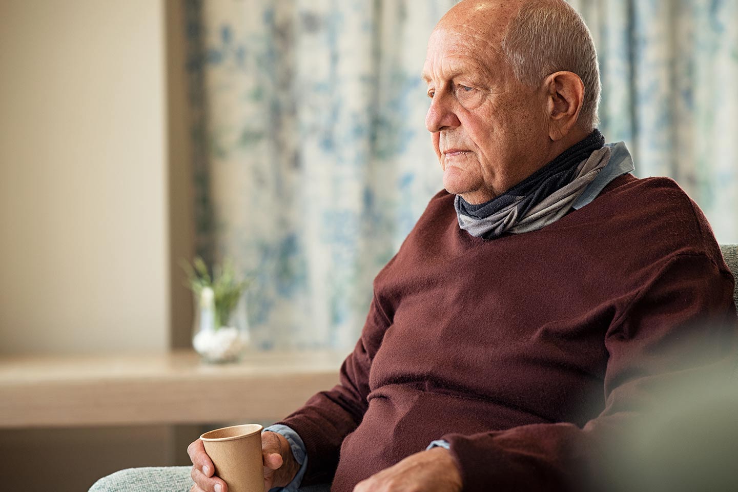 Photo of a man in a chocolate brown jumper holding a paper coffee cup