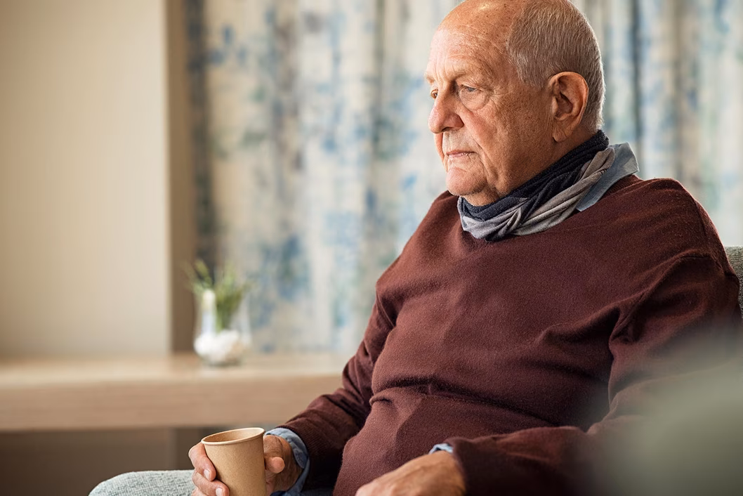 Photo of a man in a chocolate brown jumper holding a paper coffee cup