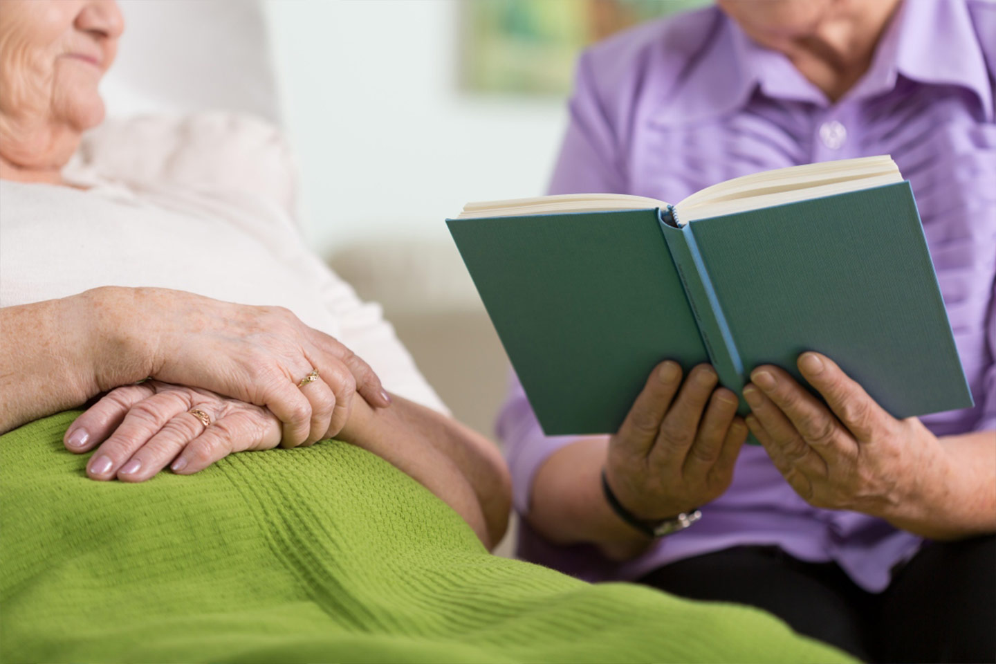 Photo of someone reading a book to a person in bed
