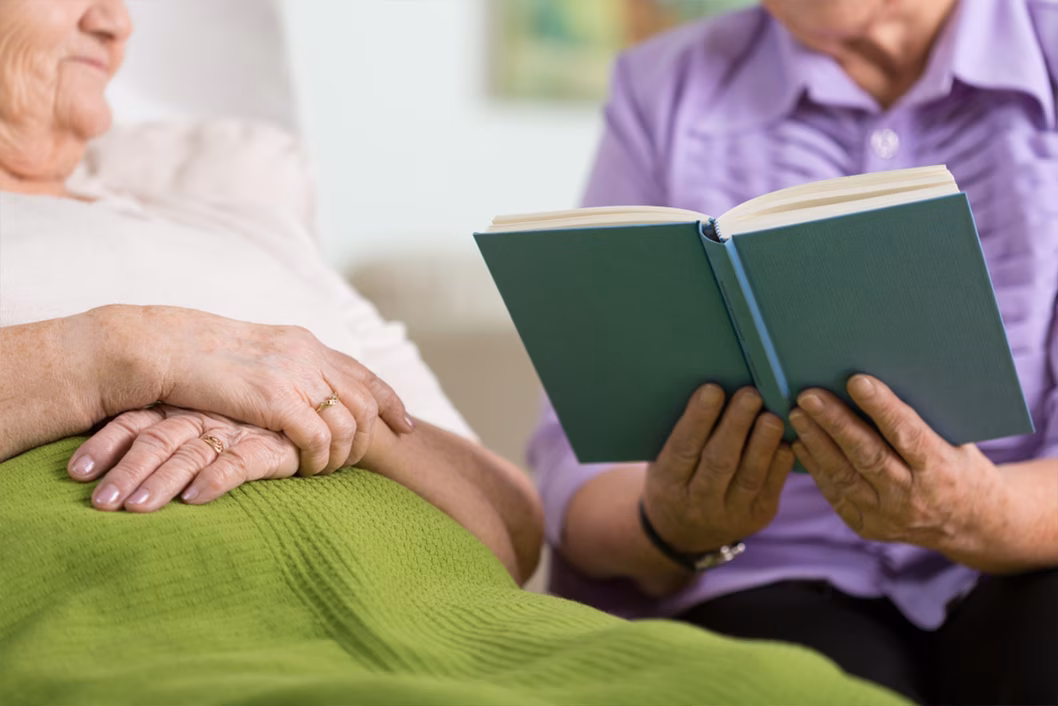 Photo of someone reading a book to a person in bed