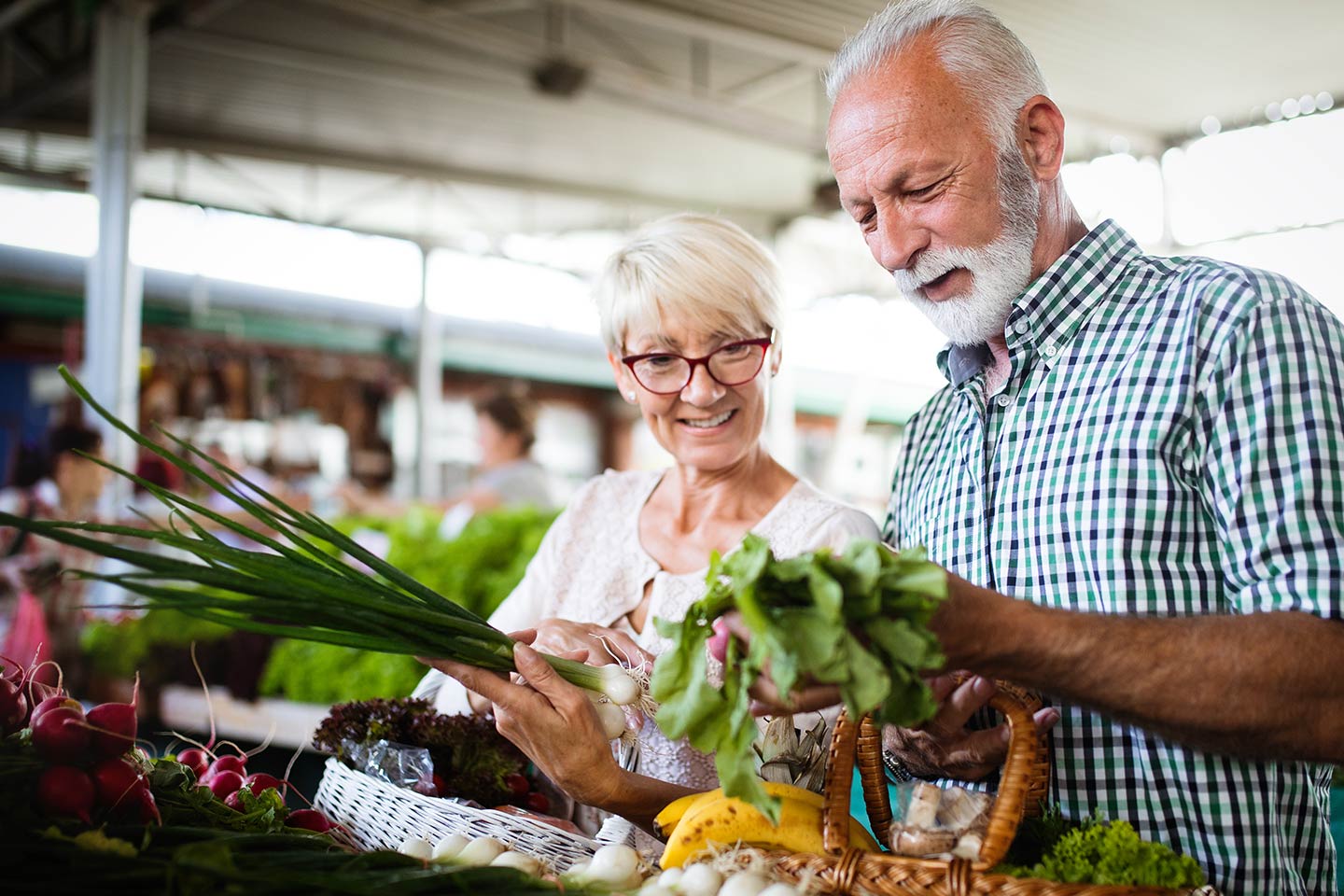 Photo of a smiling couple inspecting vegetables at a market