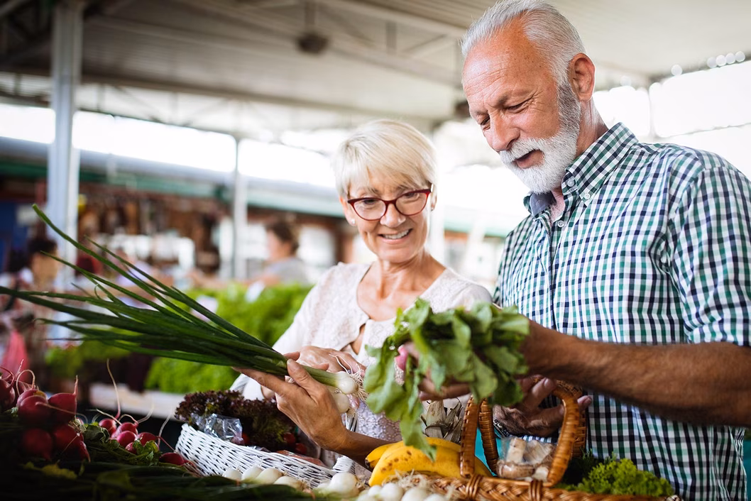 Photo of a smiling couple inspecting vegetables at a market