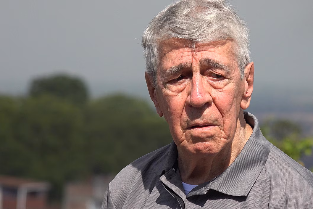 Photo of man wearing a grey polo shirt with trees in the background