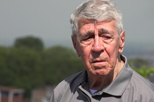 Photo of man wearing a grey polo shirt with trees in the background
