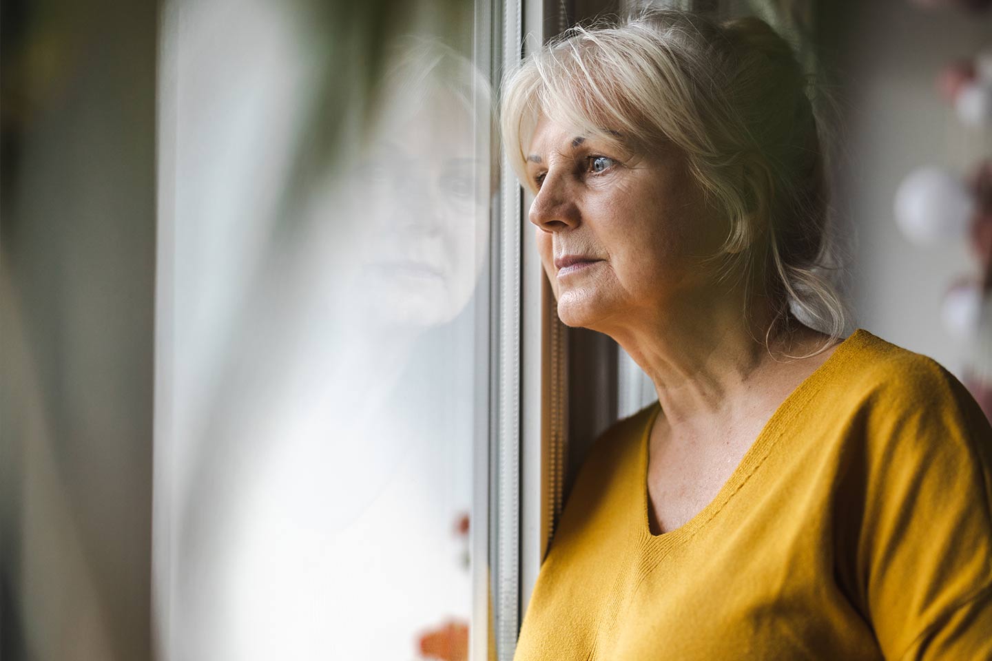 Photo of a woman in a mustard top looking out a window