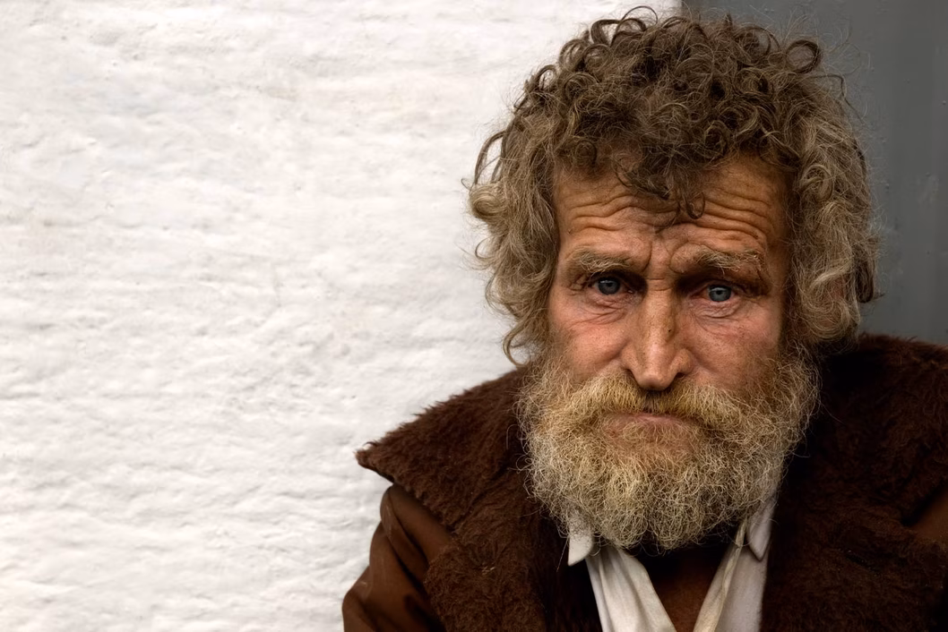Photo of a man with curly brown hair and a brown jacket