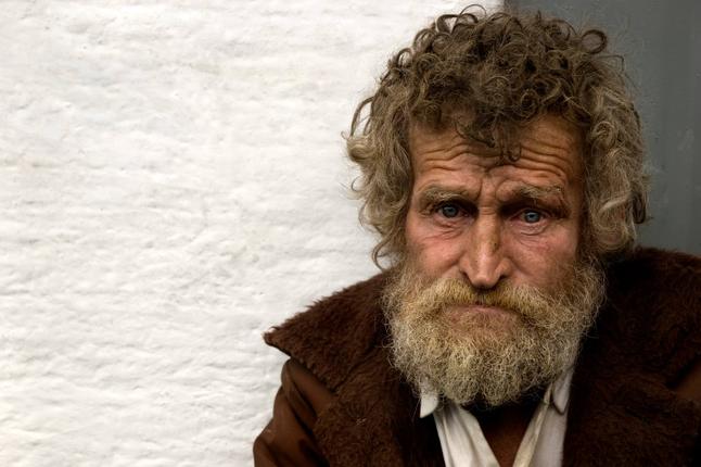 Photo of a man with curly brown hair and a brown jacket