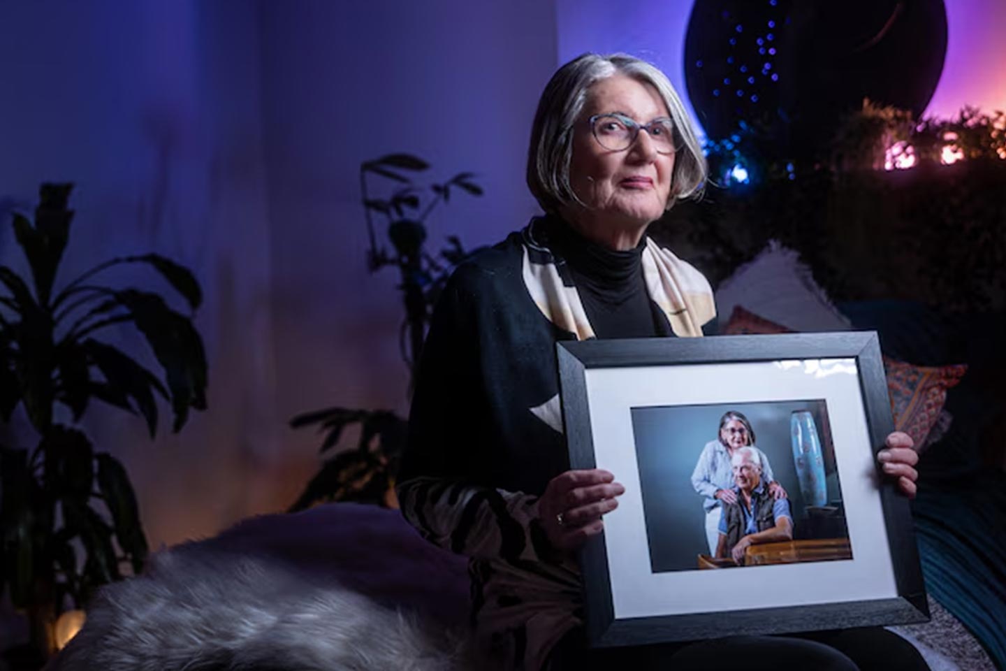 Photo of a woman in a darkened room holding a framed portrait
