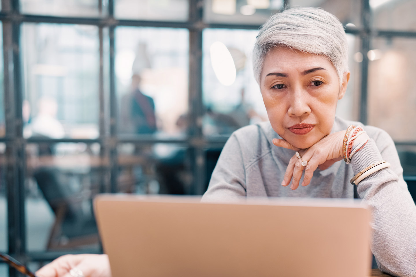 Mature Asian woman looking concerned as she looks at her laptop computer