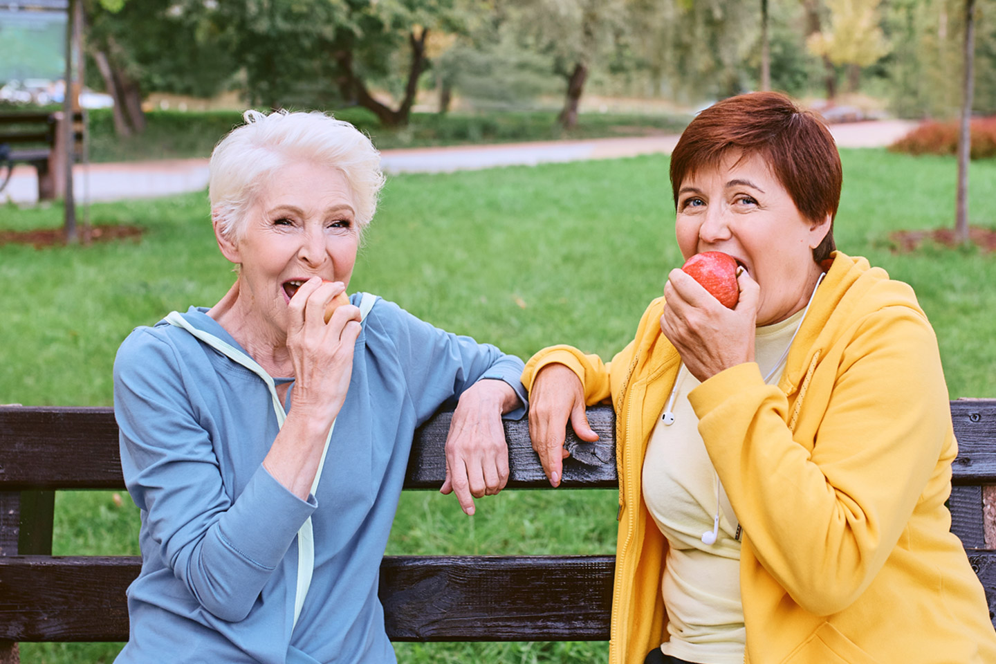 Picture of a two women sitting outside on a bench eating an apple