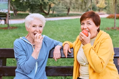 Picture of a two women sitting outside on a bench eating an apple