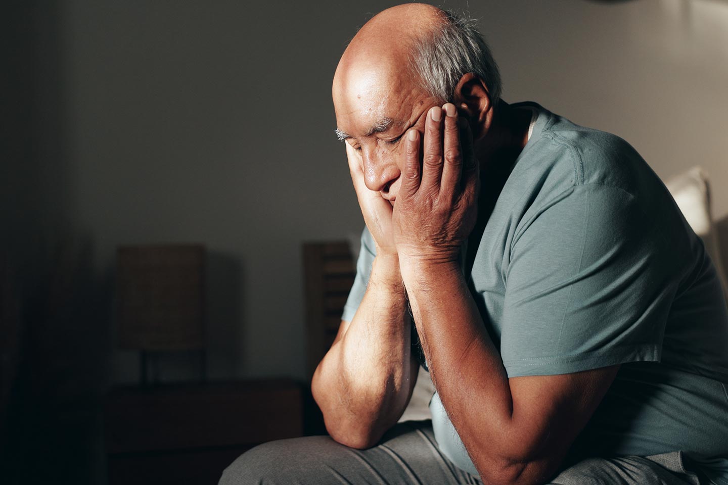 Photo of a man sitting in a dim room with his head in his hands