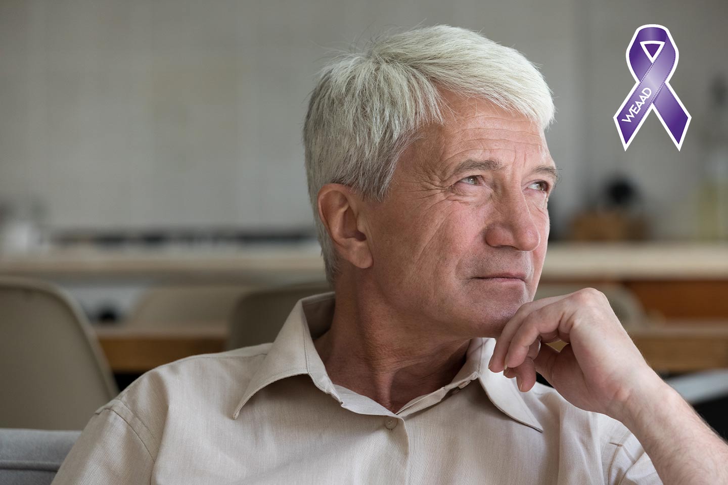 Photo of man with white hair and pale shirt resting his chin on his hand