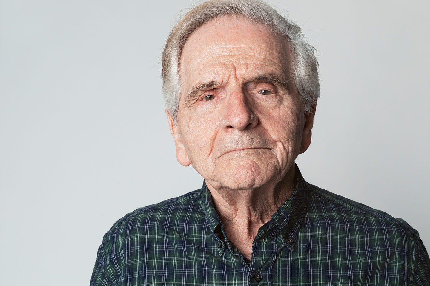Photo of a man in a green plaid shirt looking against a soft grey background