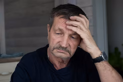 Image of an older man with a moustache and his had resting on his forehead