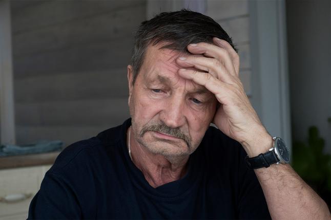 Image of an older man with a moustache and his had resting on his forehead