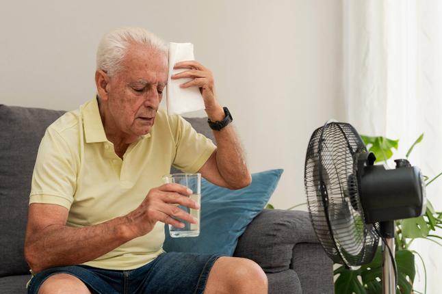 Photo of a man sitting in front of a fan with a glass of water