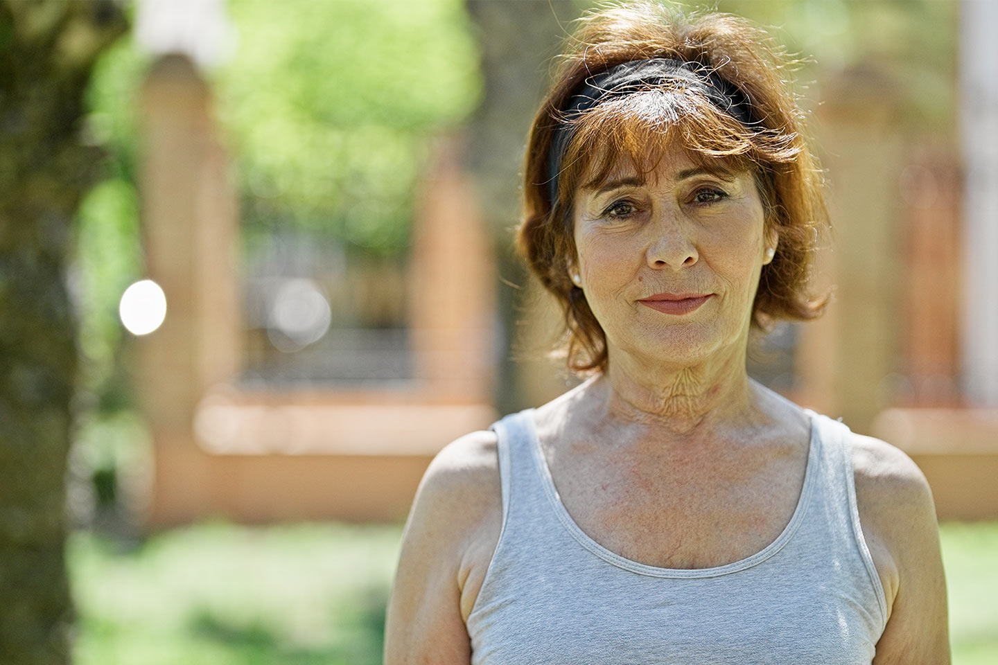 Image of an older hispanic woman who is outside on a sunny day and is wearing a light grey singlet