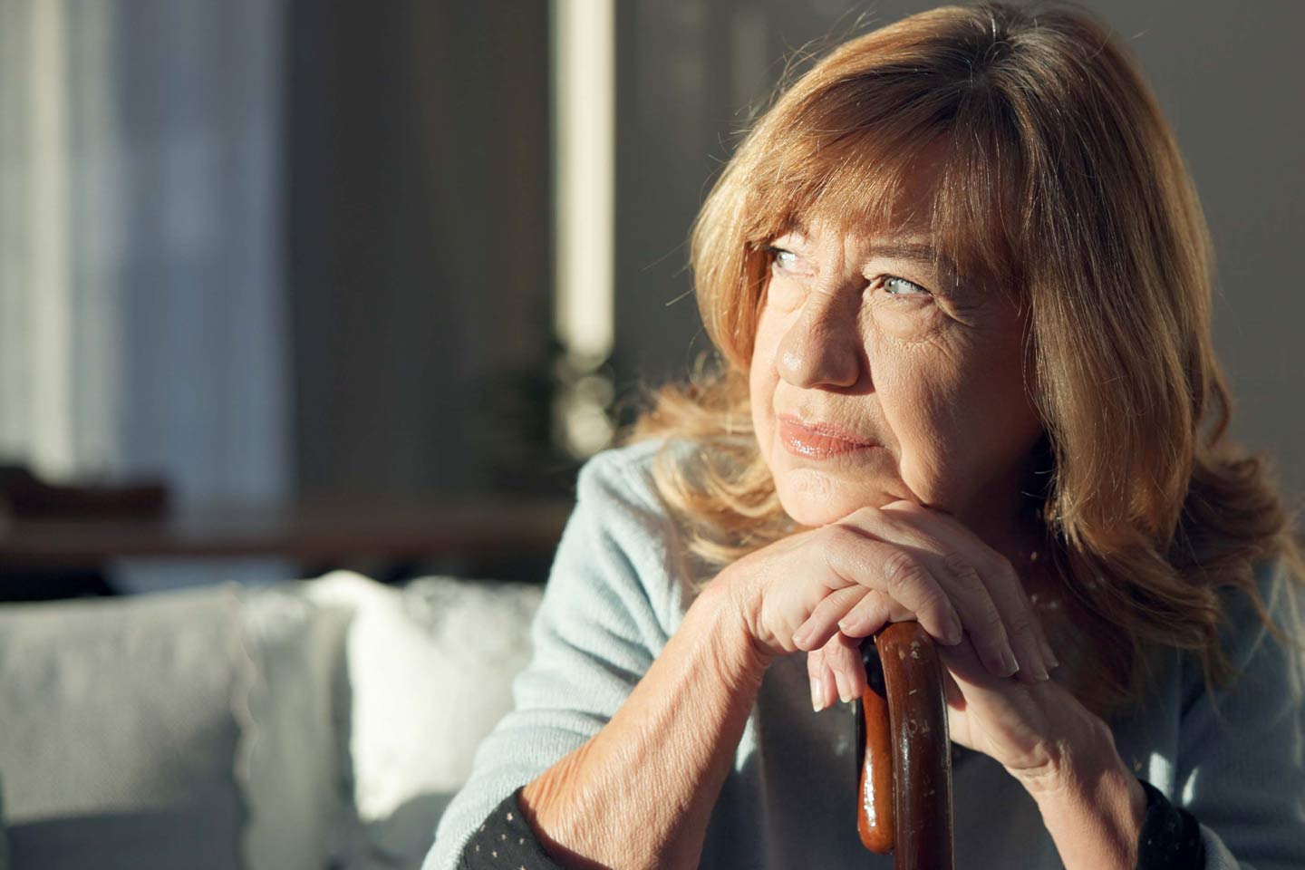 Photo of a woman with a walking stick in a sunlit room