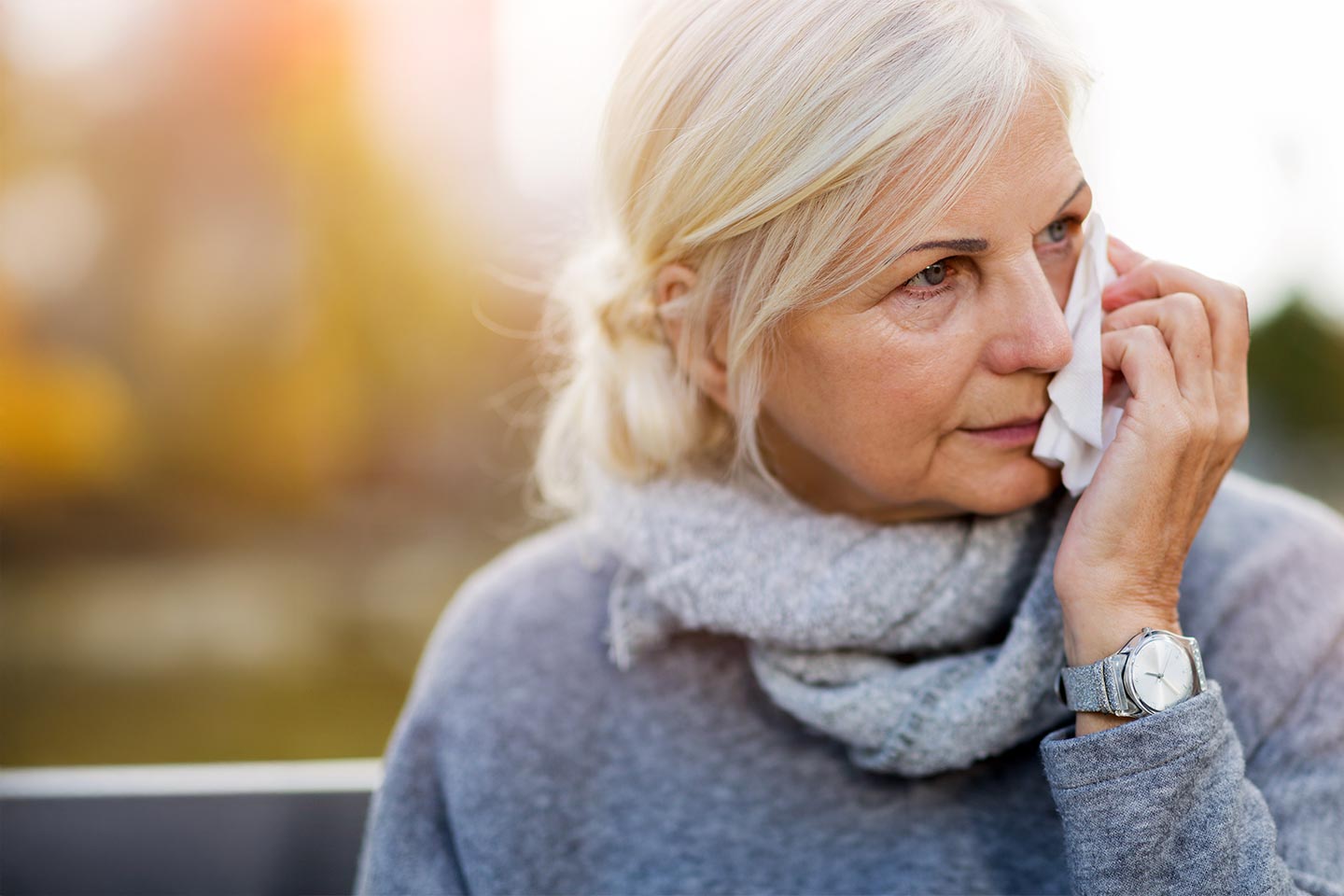 Photo of a woman in grey holding a tissue to her face