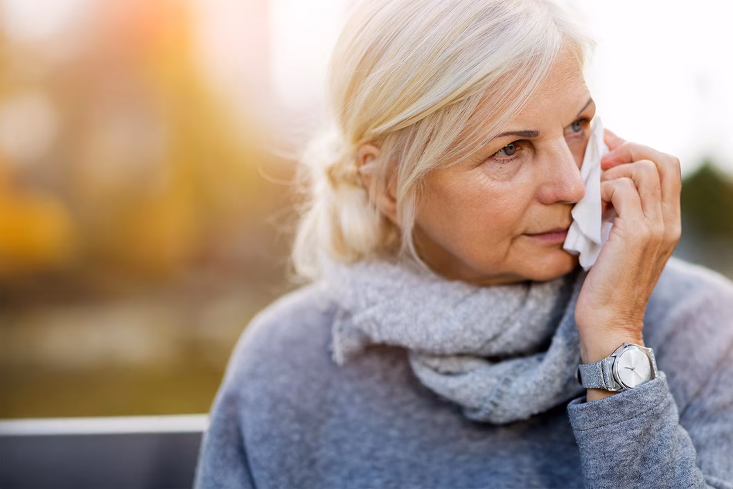 Photo of a woman in grey holding a tissue to her face