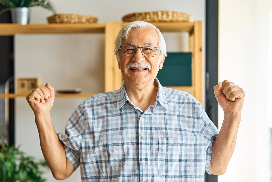 Image of an older man with both hands up by his side in a gesture of joy