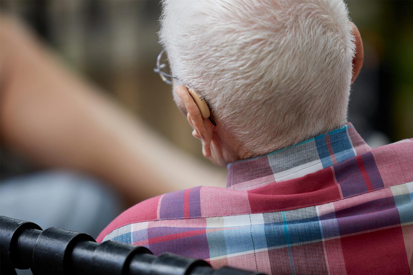 Photo of the back of an white-haired person's head with hearing aid showing