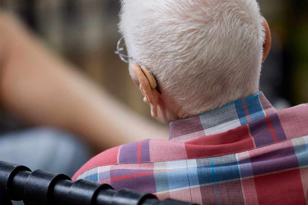 Photo of the back of an white-haired person's head with hearing aid showing