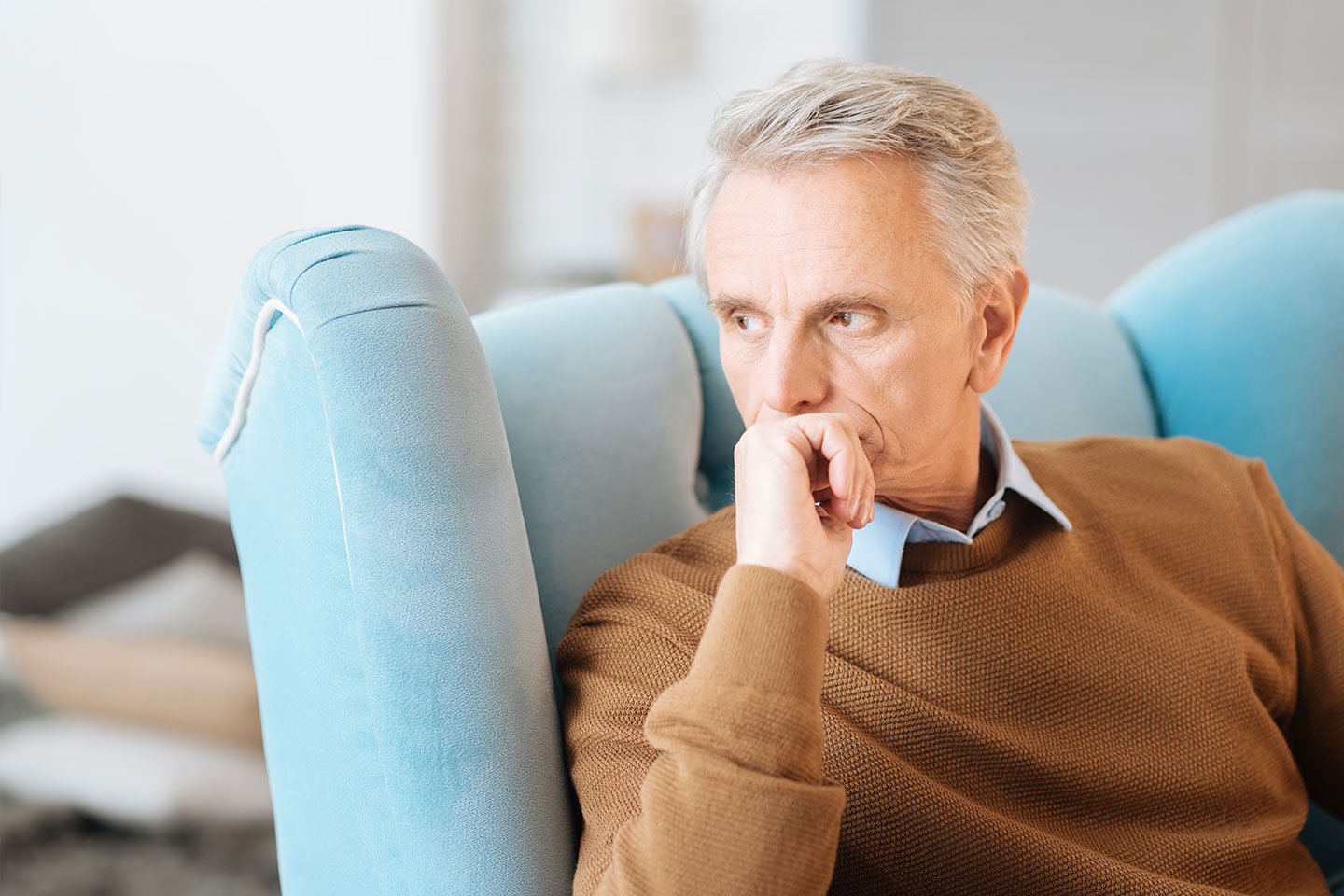 Photo of a man in a tan jumper in a blue armchair