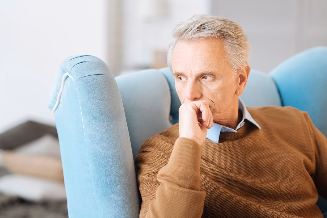 Photo of a man in a tan jumper in a blue armchair
