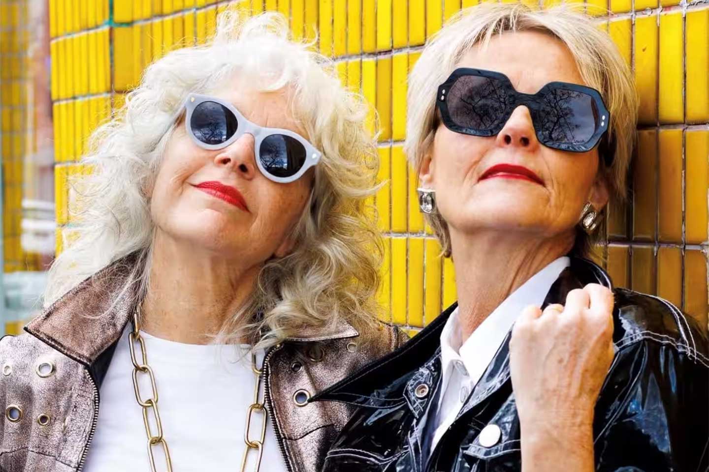 Photo of two women wearing sunglasses leaning on a yellow tiled wall