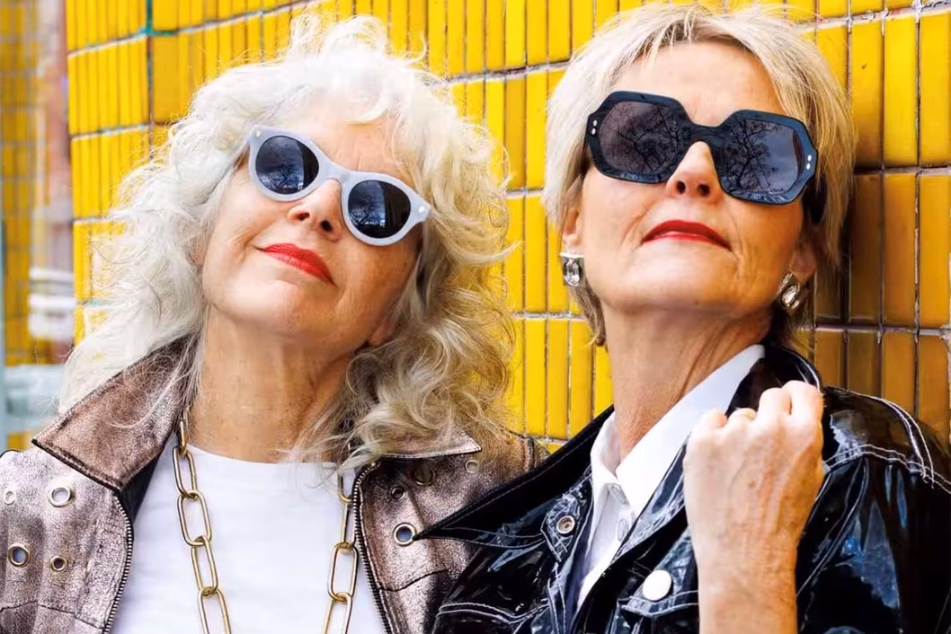 Photo of two women wearing sunglasses leaning on a yellow tiled wall