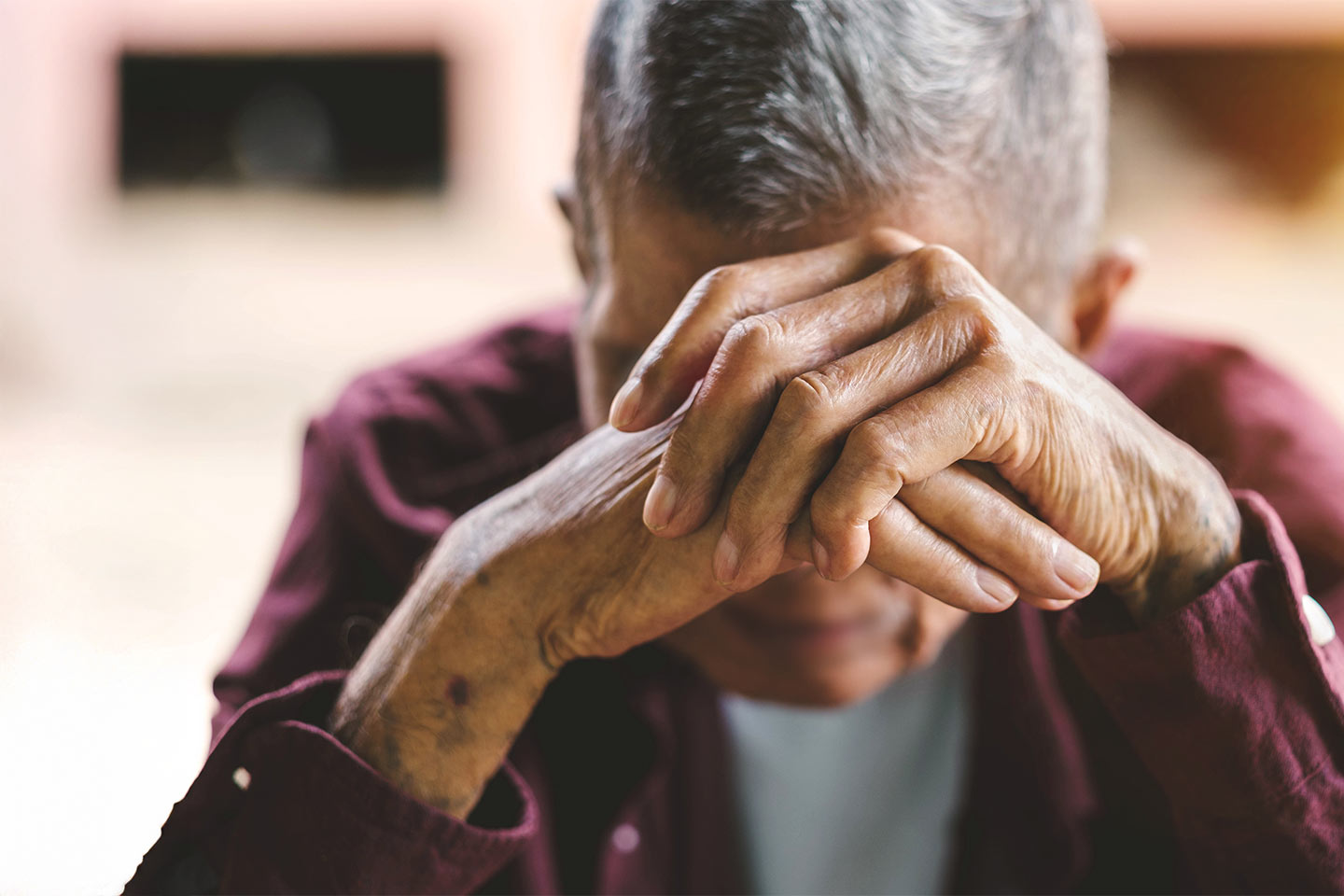 Photo of a man in a maroon shirt resting his head on his hands