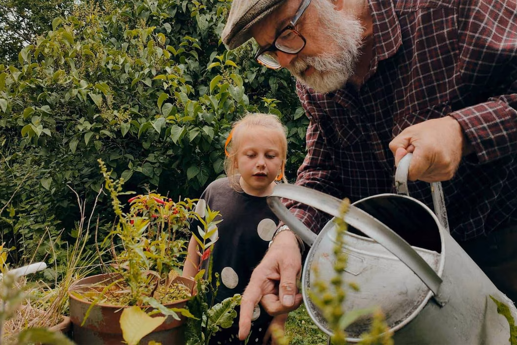 Photo in a garden of a curious child and a man with a watering can