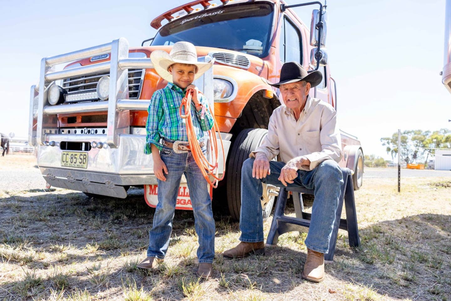 Photo of very young cowboy and his senior mentor sitting in front of a truck.