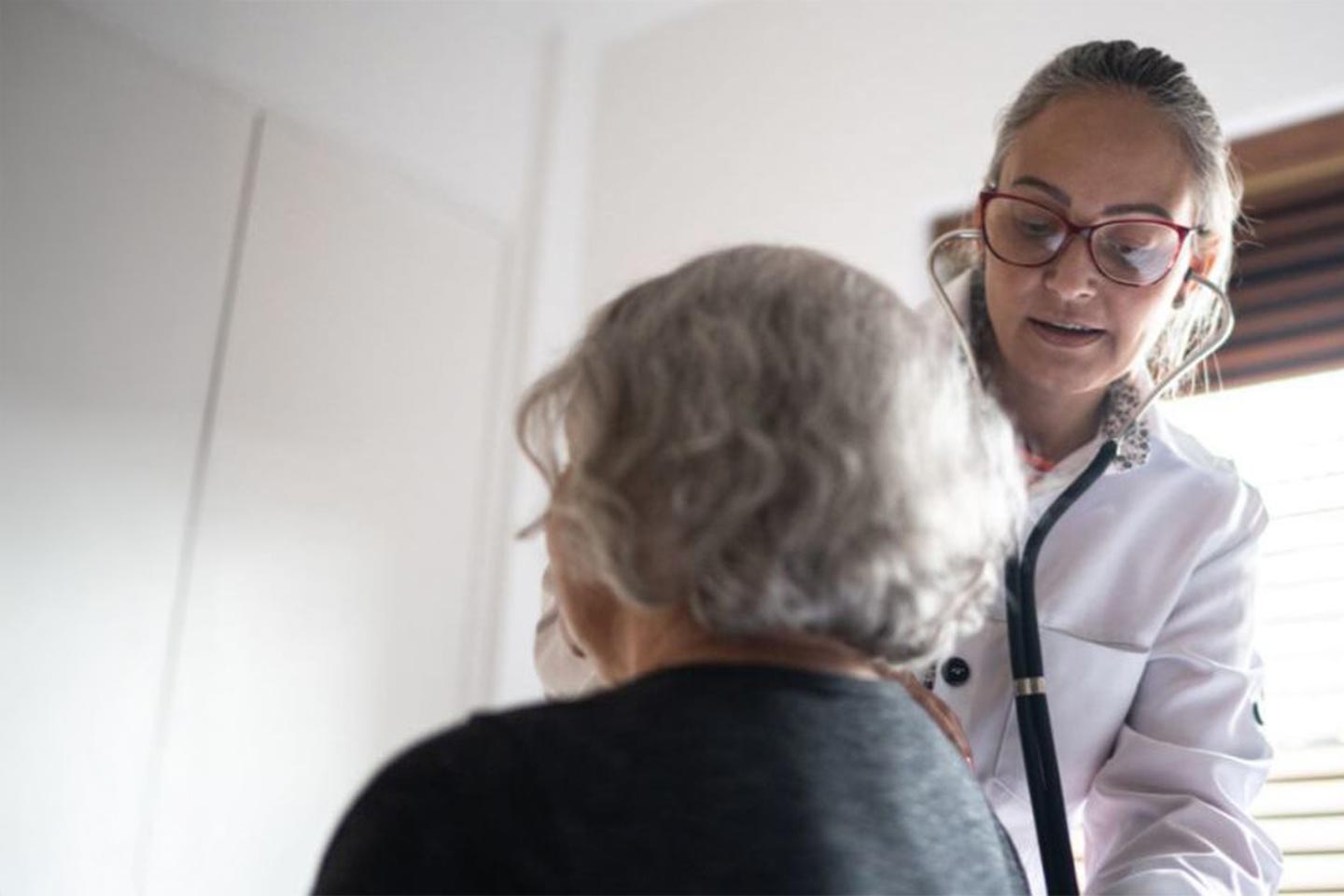 Photo of a doctor listening to a woman's back with a stethoscope